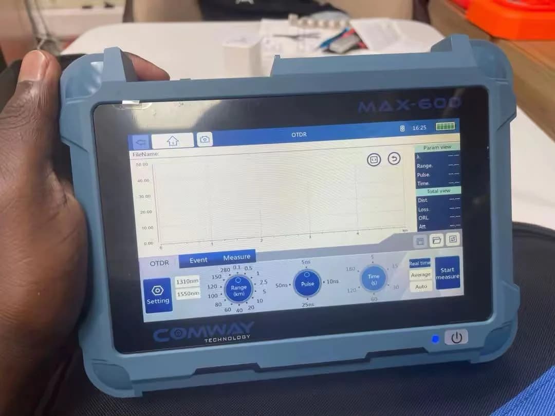 Technician holding an OTDR test set whose screen shows a fiber trace and measurement controls