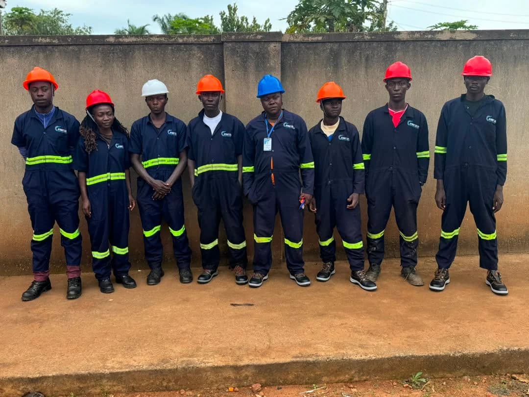 Eight Atomet crew members in navy coveralls with reflective bands and coloured hard hats standing in a line against a wall