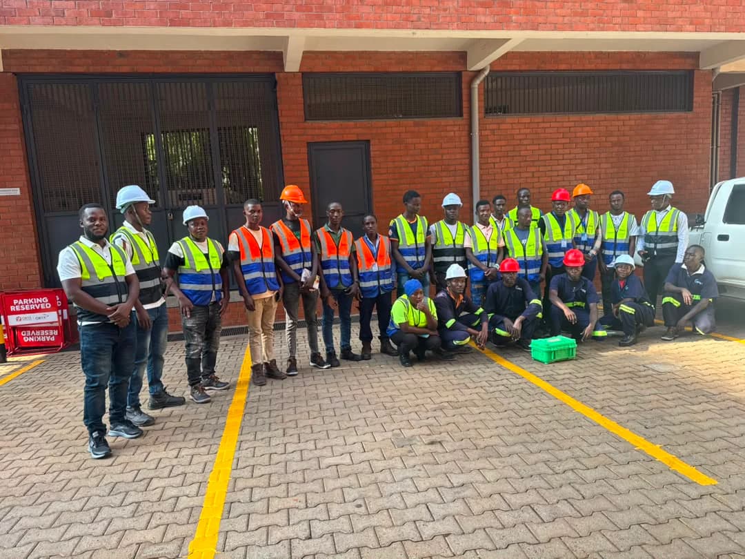 Atomet field crew of about twenty in hi-vis vests and hard hats, standing and kneeling in a paved yard in front of a brick building