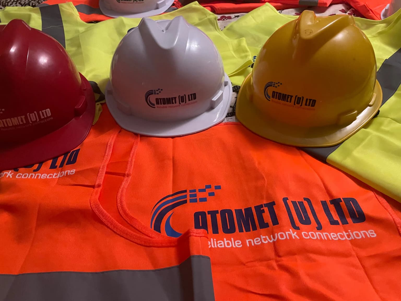 Red, white and yellow hard hats with the Atomet logo resting on orange and lime hi-vis vests printed Atomet (U) Ltd, Reliable network connections