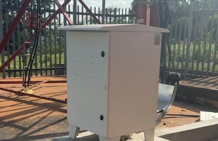 New outdoor equipment cabinet standing closed on a concrete plinth inside a fenced telecom compound