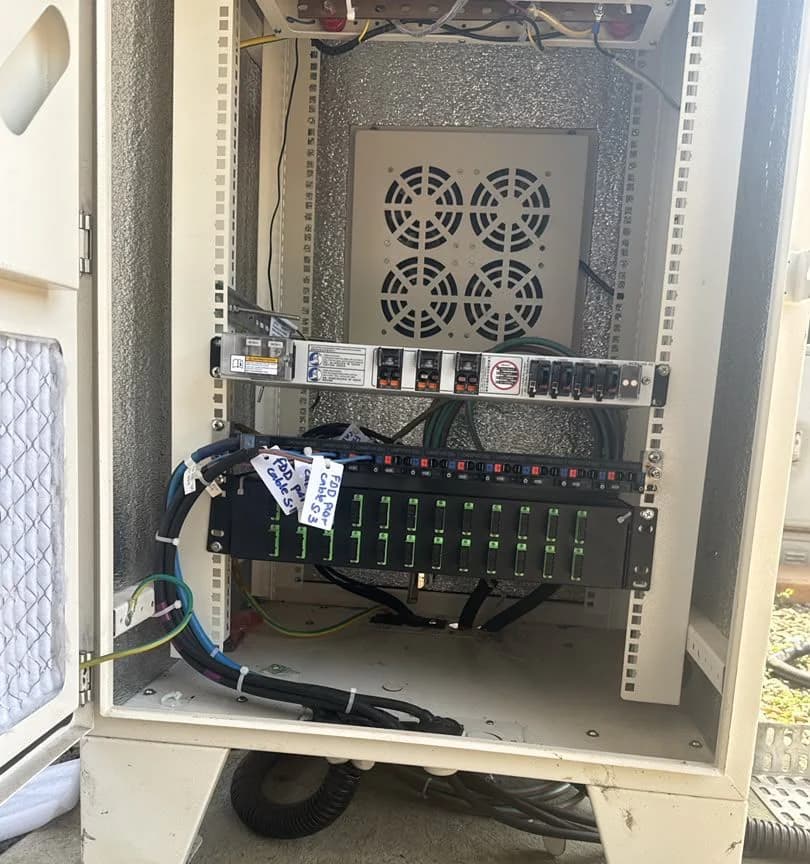 Cabinet interior with a power distribution unit, cooling fans and a row of labelled fiber adapters mounted below