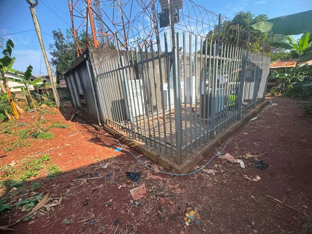 Fenced telecom compound on red soil with cabinets inside and fiber cable running in along the ground