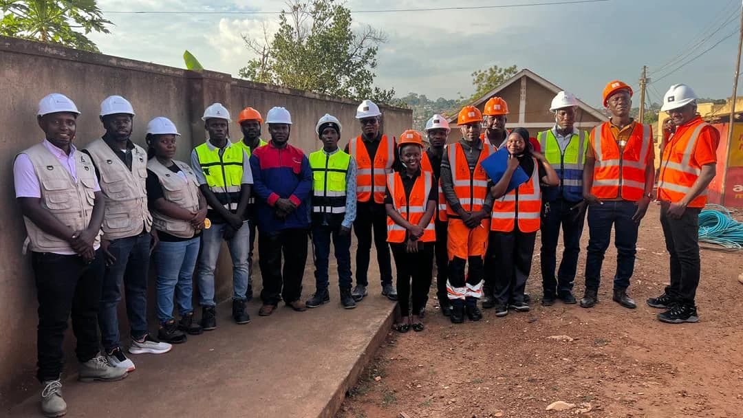 Large group of contractors and engineers in hard hats lined up along a compound wall for a joint site briefing