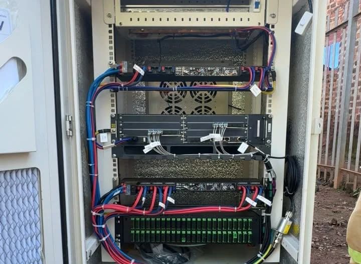 Inside an outdoor cabinet: rack equipment with neatly dressed red and blue power leads and a full row of green SC fiber adapters