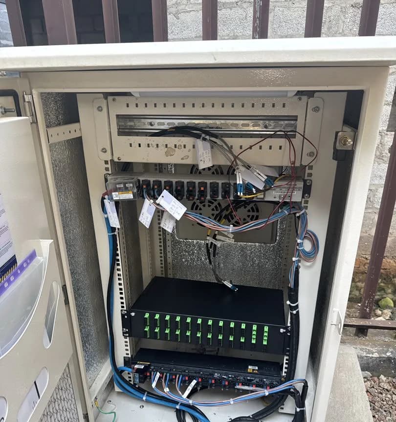 Open cabinet showing a rack-mounted fiber patch panel with labelled pigtails and coiled black ducting below