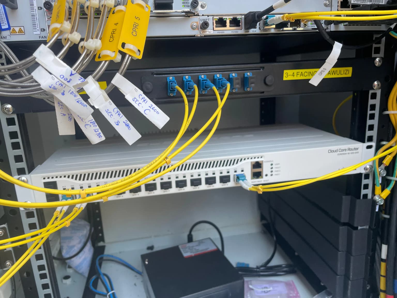Rack-mounted network equipment with yellow fiber uplinks, each lead tagged with a handwritten label