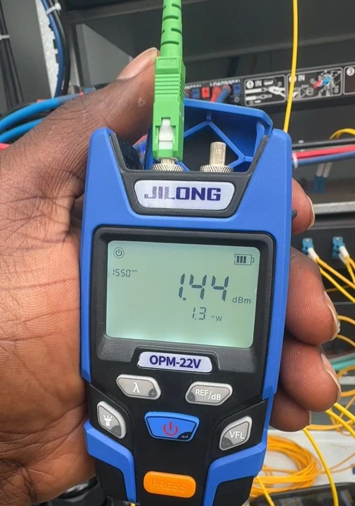 Hand holding an optical power meter connected to a green SC connector, the display reading the received light level