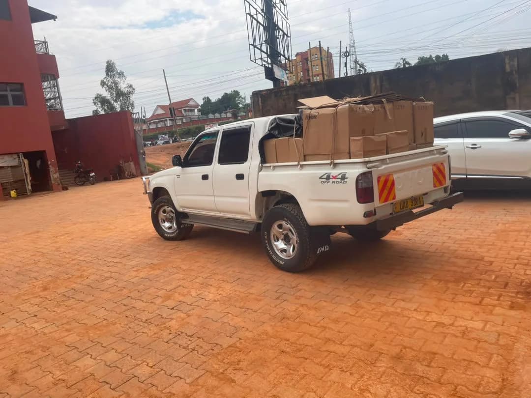 White double-cab pickup loaded with boxed materials parked on red brick paving