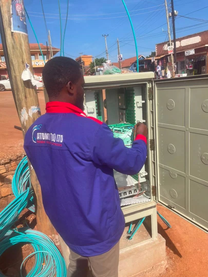 Atomet technician in a company jacket patching drop fibers inside a roadside distribution cabinet on a busy trading street