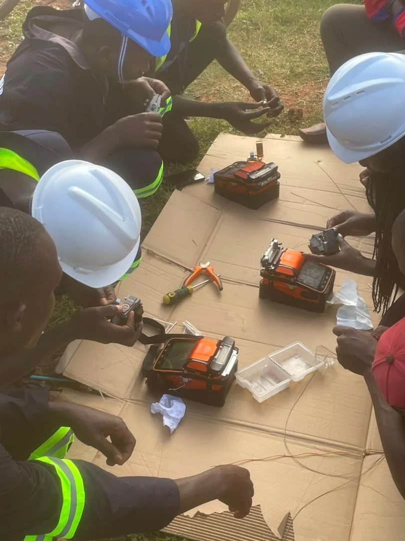Technicians in hard hats crouched over cardboard practising with orange fusion splicers