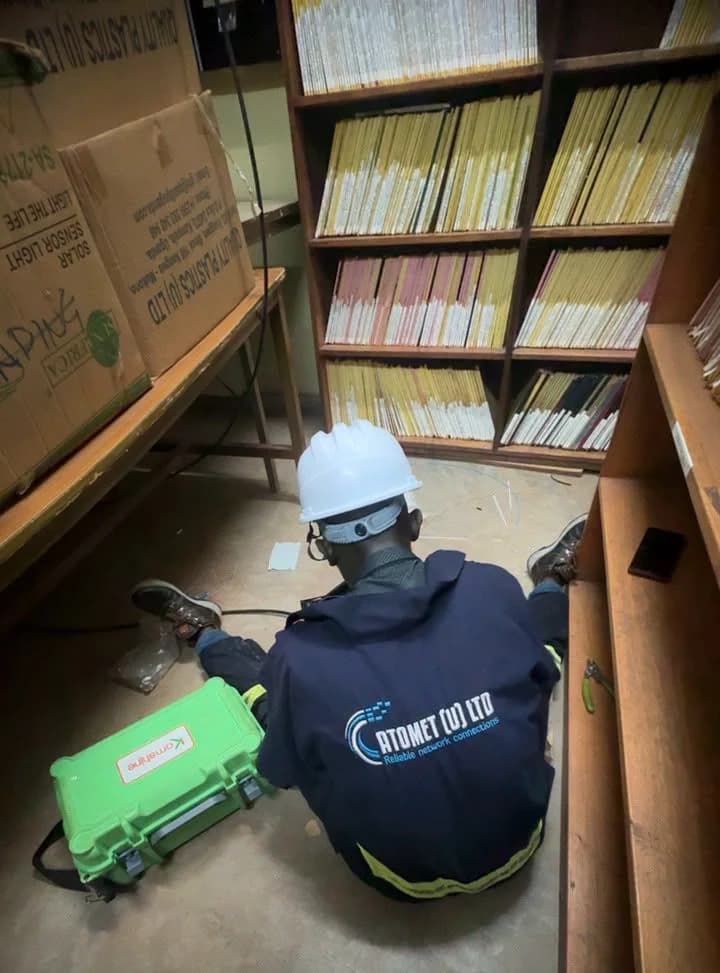 Atomet technician in a white hard hat working at floor level beside a bookshelf with a green equipment case
