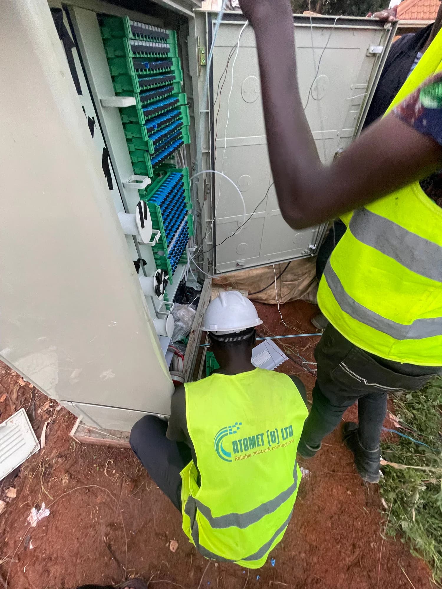Atomet technician crouching at the base of an open distribution hub while a colleague patches the adapter field above